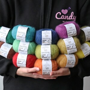 May include: A collection of colorful yarn skeins, each labeled "GAZZAL SUPER KID MOHAIR", arranged in a pyramid shape. The yarn is soft and fluffy, perfect for knitting or crocheting.