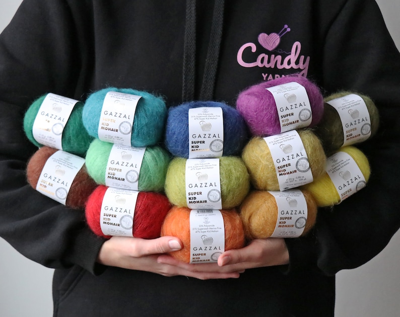 May include: A collection of colorful yarn skeins, each labeled "GAZZAL SUPER KID MOHAIR", arranged in a pyramid shape. The yarn is soft and fluffy, perfect for knitting or crocheting.