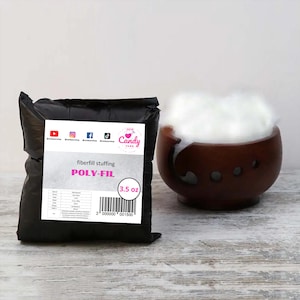 May include: A black bag of Poly-Fil fiberfill stuffing, with a white label that reads "fiberfill stuffing POLY-FIL" and "3.5 oz". A wooden bowl is filled with fluffy white fiberfill. The background is a light wood surface.