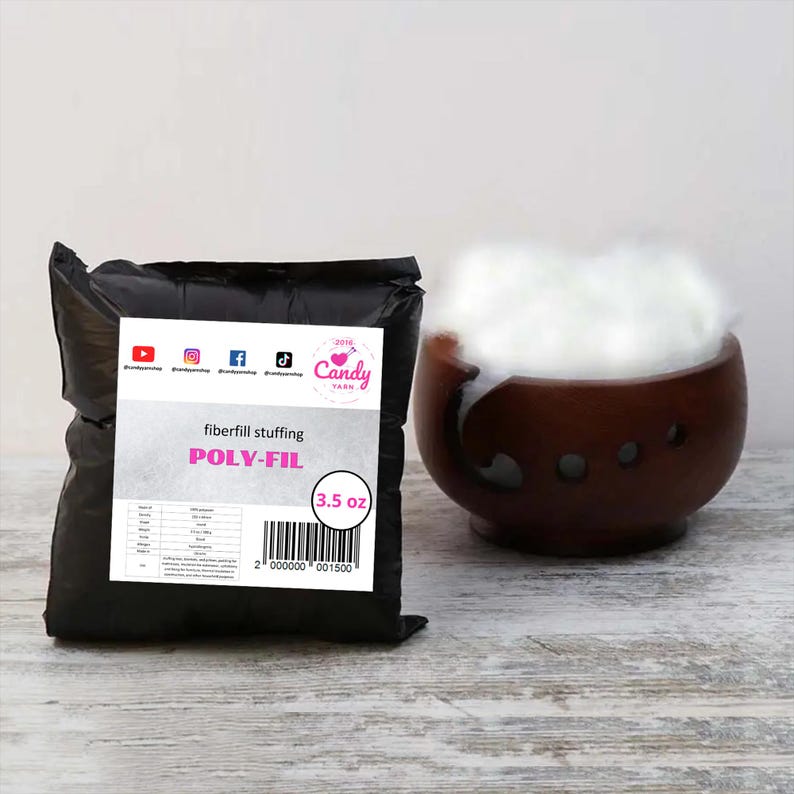 May include: A black bag of Poly-Fil fiberfill stuffing, with a white label that reads "fiberfill stuffing POLY-FIL" and "3.5 oz". A wooden bowl is filled with fluffy white fiberfill. The background is a light wood surface.