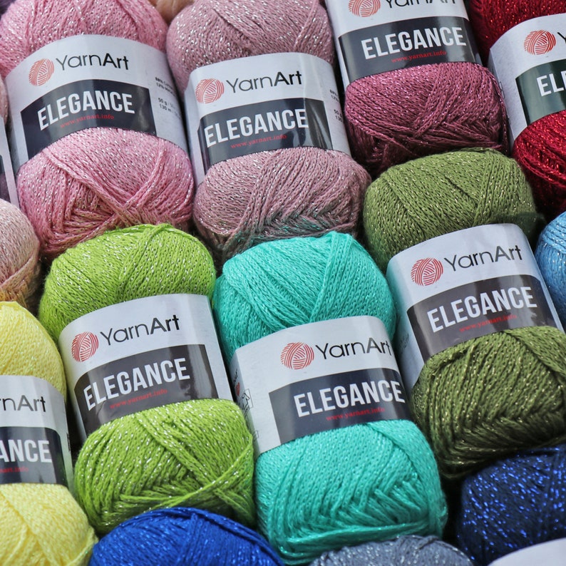 May include: Assortment of YarnArt Elegance yarn skeins in various colors, including pink, green, blue, and turquoise. Each skein features a white label with the brand name and yarn type.