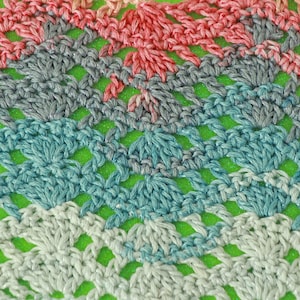 May include: Close-up of a crocheted fabric with a repeating pattern of squares. The fabric is made with yarn in shades of pink, gray, blue, and white.