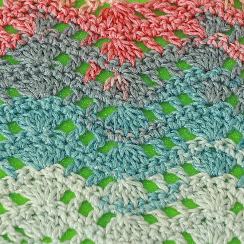 May include: Close-up of a crocheted fabric with a repeating pattern of squares. The fabric is made with yarn in shades of pink, gray, blue, and white.