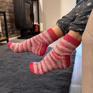 Può includere: Un paio di calzini a crochet a righe rosa e bianche. I calzini sono realizzati con una maglia testurizzata e hanno un polsino a coste.