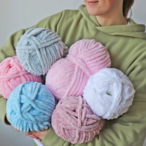 K&ouml;nnte beinhalten: Sechs Kn&auml;uel Garn in verschiedenen Farben, darunter rosa, blau, wei&szlig; und grau. Das Garn ist weich und flauschig und perfekt zum Stricken oder H&auml;keln.