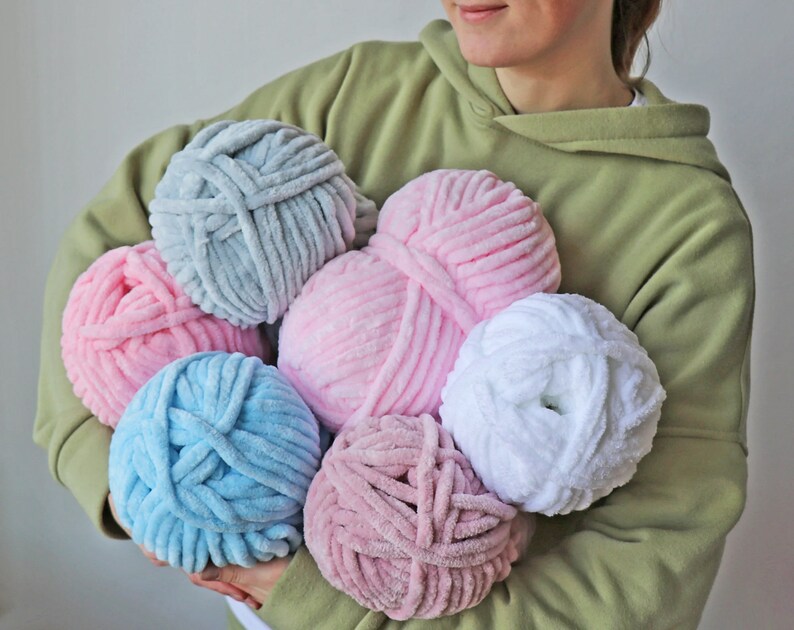 K&ouml;nnte beinhalten: Sechs Kn&auml;uel Garn in verschiedenen Farben, darunter rosa, blau, wei&szlig; und grau. Das Garn ist weich und flauschig und perfekt zum Stricken oder H&auml;keln.