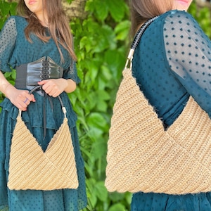 Puede incluir: Un bolso de mano de crochet de color beige con asas de cuero negro. El bolso se lleva sobre el hombro de una persona que lleva un vestido verde con lunares.