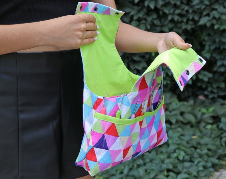 May include: A colorful geometric fabric bag with a lime green lining and multiple pockets. The bag is open and has various knitting needles and tools inside.