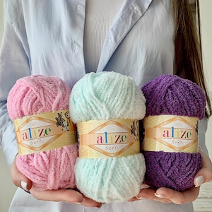May include: Three skeins of yarn in pink, light blue, and purple. Each skein has a label that reads "Baby Alize Softy".