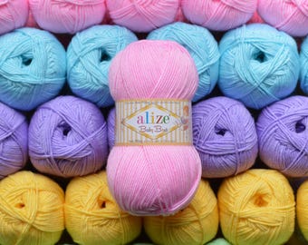 Puede incluir: Una colección de ovillos de lana coloridos en tonos rosa, azul, morado, amarillo y verde. Un ovillo rosa con una etiqueta que dice "alize Baby Best" en primer plano. La lana es para tejer o hacer ganchillo.