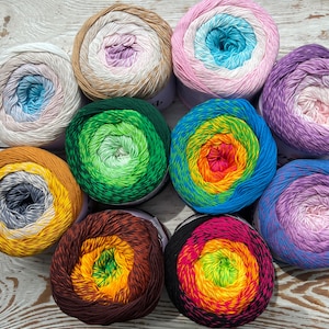 May include: Ten balls of yarn in various colors and patterns, including green, blue, orange, pink, and purple. The yarn is arranged in a circle on a white wooden surface.