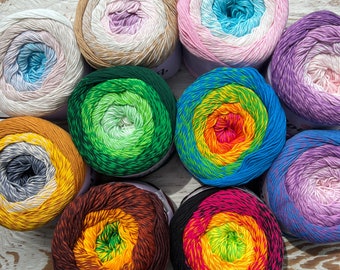 May include: Ten balls of yarn in various colors and patterns, including green, blue, orange, pink, and purple. The yarn is arranged in a circle on a white wooden surface.