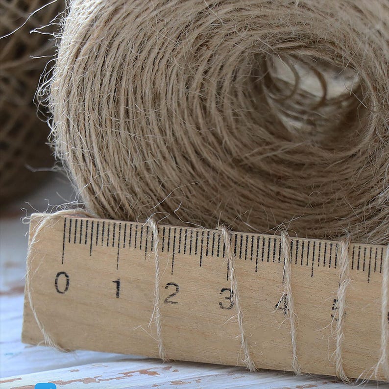 K&ouml;nnte beinhalten: Nahaufnahme einer Rolle Naturbastgarn oder Jutegarn, mit einem Holzlineal, das 12,7 cm lang ist. Das Garn ist braun und hat eine raue Textur.