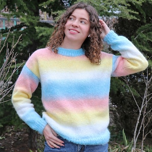 May include: A pastel striped sweater with a fuzzy texture. The sweater has horizontal stripes of pink, yellow, blue, and white.