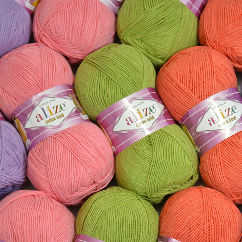Puede incluir: Una colecci&oacute;n de ovillos de lana coloridos en tonos rosa, verde, naranja y morado. Cada ovillo est&aacute; etiquetado con "alize Cotton Gold" en una etiqueta morada y blanca. La lana parece suave y adecuada para varios proyectos de tejido o ganchillo.