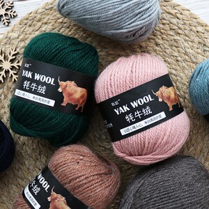 May include: Six balls of yarn in different colors, including green, pink, brown, gray, and blue. Each ball has a label with the text "YAK WOOL" and "牦牛绒" in Chinese characters. The label also includes the text "正心理人心,来自高原的爱" in Chinese characters, which translates to "Warm the heart with sincerity, love from the plateau."