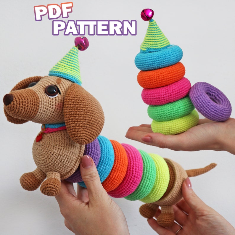 May include: A crocheted dachshund toy wearing a party hat with a bell on top. The dachshund's tail is a stack of colorful crocheted rings that can be removed and stacked.