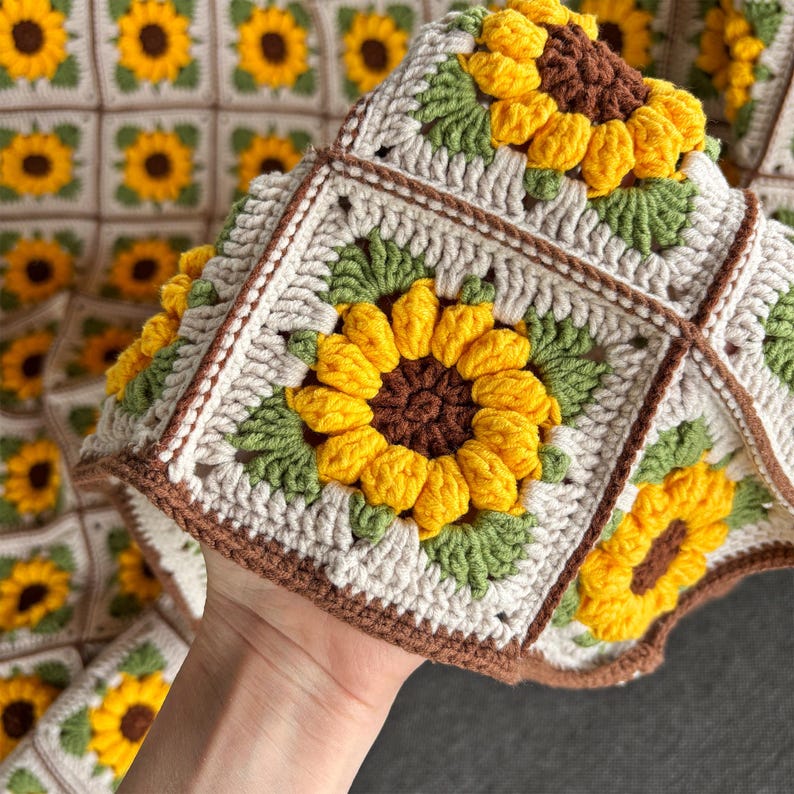 May include: A crocheted blanket with a sunflower pattern. The blanket is made of beige, brown, green, and yellow yarn. The sunflowers are made with a raised stitch technique.