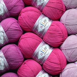 Puede incluir: Primer plano de varias madejas de hilo Alize Cotton Gold en varios tonos de rosa y morado. El hilo est&aacute; bien enrollado y las etiquetas son visibles, indicando la marca y el tipo de hilo. Ideal para proyectos de punto y ganchillo.