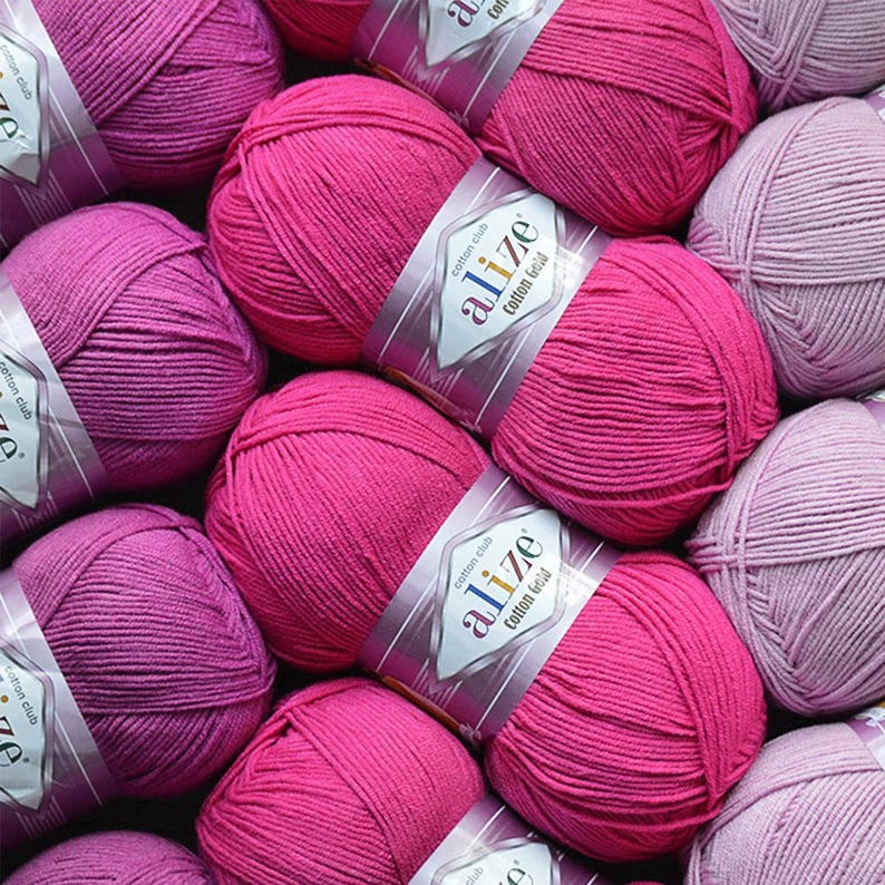 Puede incluir: Primer plano de varias madejas de hilo Alize Cotton Gold en varios tonos de rosa y morado. El hilo est&aacute; bien enrollado y las etiquetas son visibles, indicando la marca y el tipo de hilo. Ideal para proyectos de punto y ganchillo.