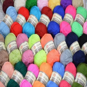 Puede incluir: Una colección de madejas de hilo coloridas en varios tonos, incluyendo azul, rojo, rosa, verde y naranja. Cada madeja está etiquetada con "YarnArt". El hilo está dispuesto de forma compacta, creando una exhibición vibrante y texturizada.