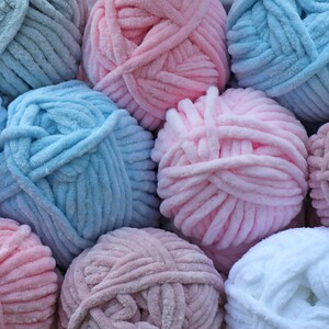 K&ouml;nnte beinhalten: Eine Sammlung von Wollkn&auml;uel in verschiedenen Farben, darunter Rosa, Blau und Wei&szlig;. Die Wolle ist weich und flauschig, und die Kn&auml;uel sind kreisf&ouml;rmig angeordnet.