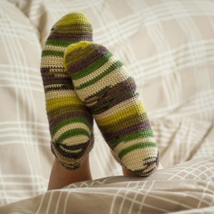 Könnte beinhalten: Ein Paar grün-braune gestreifte gehäkelte Socken. Die Socken sind getragen und die Zehen sind sichtbar.