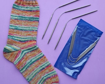 May include: A colorful striped sock with a green, orange, and pink color scheme. The sock is lying on a purple surface next to a package of four silver knitting needles.