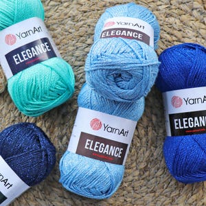 May include: Four balls of YarnArt Elegance yarn in blue, teal, dark blue, and light blue. Each ball has a white label with the YarnArt logo and the text "Elegance" on it.