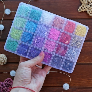 May include: A clear plastic storage box filled with small colourful beads. The box has 24 compartments, each filled with a different colour of beads. The beads are arranged in rows and columns.