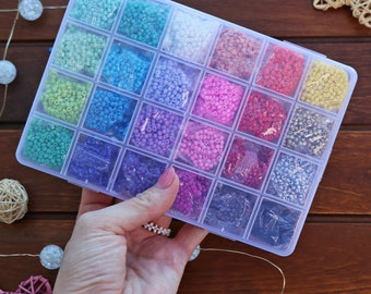 May include: A clear plastic storage box filled with small colourful beads. The box has 24 compartments, each filled with a different colour of beads. The beads are arranged in rows and columns.