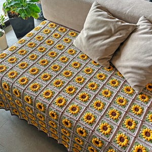 K&ouml;nnte beinhalten: Eine handgefertigte H&auml;keldecke mit einem sich wiederholenden Sonnenblumenmuster. Die Decke besteht aus Quadraten mit gelben Sonnenblumen, braunen Zentren und gr&uuml;nen Bl&auml;ttern. Der Hintergrund ist hellgrau.
