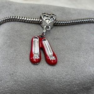 May include: A silver charm bracelet with a red and silver shoe charm. The charm is shaped like a pair of red shoes with silver bows and silver detailing.