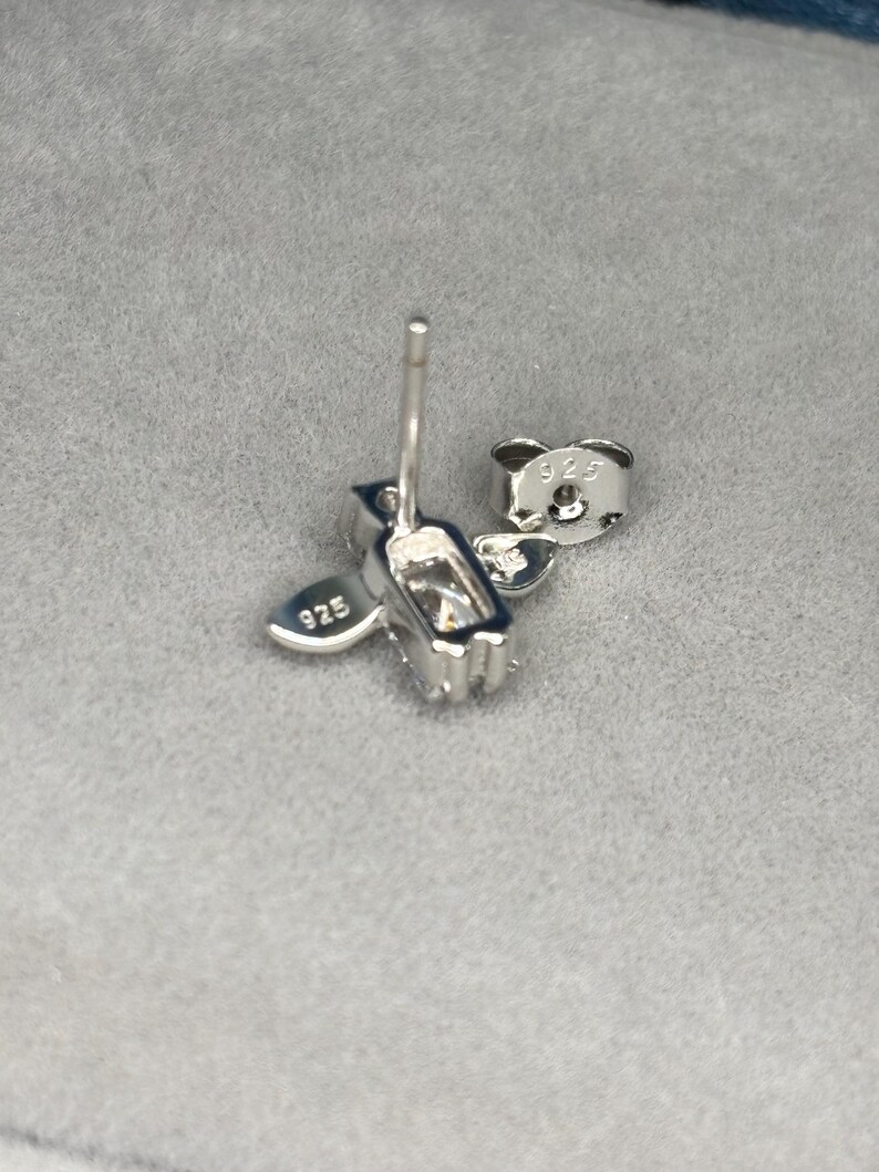 May include: Silver earrings with a heart and a rectangular shape. The earrings are marked with "925" on the back.