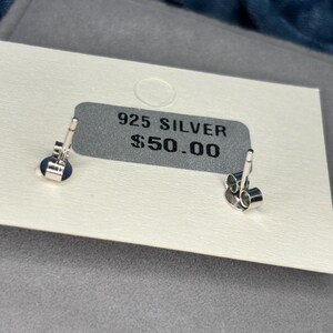 May include: A white card with the text "925 SILVER $50.00" printed on it. Two silver earring backs are visible on the card.