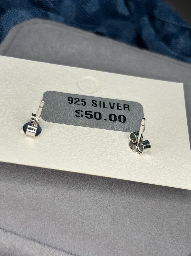 May include: A white card with the text "925 SILVER $50.00" printed on it. Two silver earring backs are visible on the card.