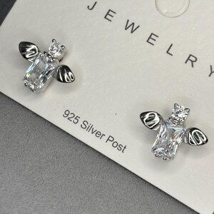 May include: A pair of silver bee earrings with clear cubic zirconia stones. The earrings are on a white card with the word "JEWELRY" and "925 Silver Post" printed on it.
