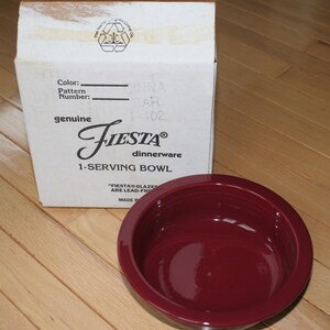 May include: A deep red Fiesta 1-serving bowl next to its original cardboard box. The box is white with the Fiesta logo and text. The bowl is round and has a glossy finish. The box reads "genuine Fiesta dinnerware".