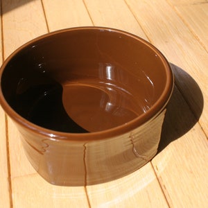 May include: A brown ceramic bowl with a smooth, glossy finish. The bowl is empty and sits on a wooden surface.