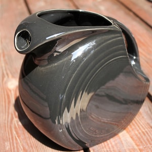 May include: A dark gray ceramic pitcher with a smooth, glossy finish. The pitcher has a wide, round base and a narrow spout.