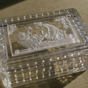 May include: A clear glass box with a raised, frosted design of a woman pushing a wheelbarrow. The box has a grid pattern on the sides.