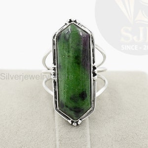 May include: A silver ring with a green and purple gemstone set in a hexagonal bezel. The ring has a delicate, intricate design.