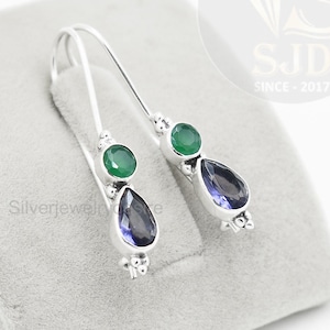 以下が含まれることがあります： シルバーのドロップデザインのイヤリングのペア。各イヤリングは、丸い緑色の石と、涙の形をした濃い青色の石が特徴です。イヤリングは灰色の表面に表示されています。