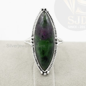 Pode incluir: Um anel de prata com uma gema oval verde e rosa engastada em uma moldura de prata. O anel está em um expositor de veludo branco.