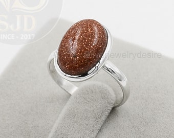 May include: A silver ring with a brown oval-shaped gemstone. The gemstone has a speckled texture.