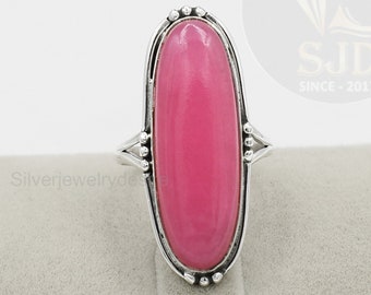 May include: A silver ring with a large oval pink gemstone. The ring has a decorative border of small beads around the gemstone.