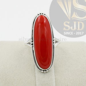 Pode incluir: Um anel de prata com uma grande pedra de coral vermelho de forma oval. O anel tem um design delicado e adornado.