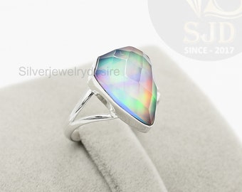 Op de afbeelding: Een zilveren ring met een grote, regenboogkleurige edelsteen in de vorm van een diamant. De ring ligt op een grijze fluwelen displaystandaard.