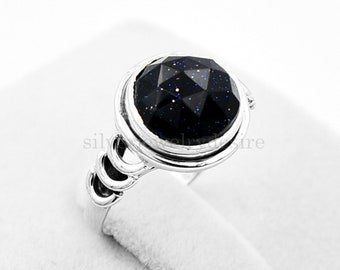 Puede incluir: Un anillo de plata con una piedra preciosa azul engastada en un engaste de bisel. El anillo tiene una banda decorativa con tres bucles.