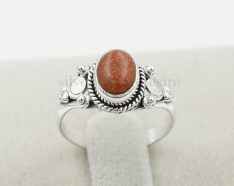 May include: A silver ring with a brown oval gemstone set in a decorative silver band. The ring has a delicate design with small silver beads and a twisted wire detail.